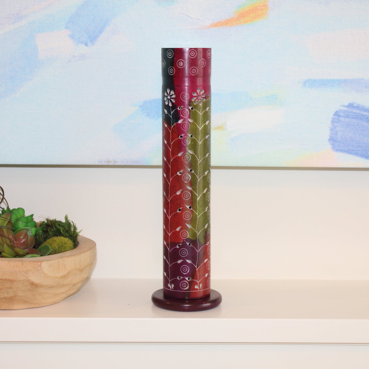 Decorative cylindrical object on a shelf with a colorful abstract painting in the background