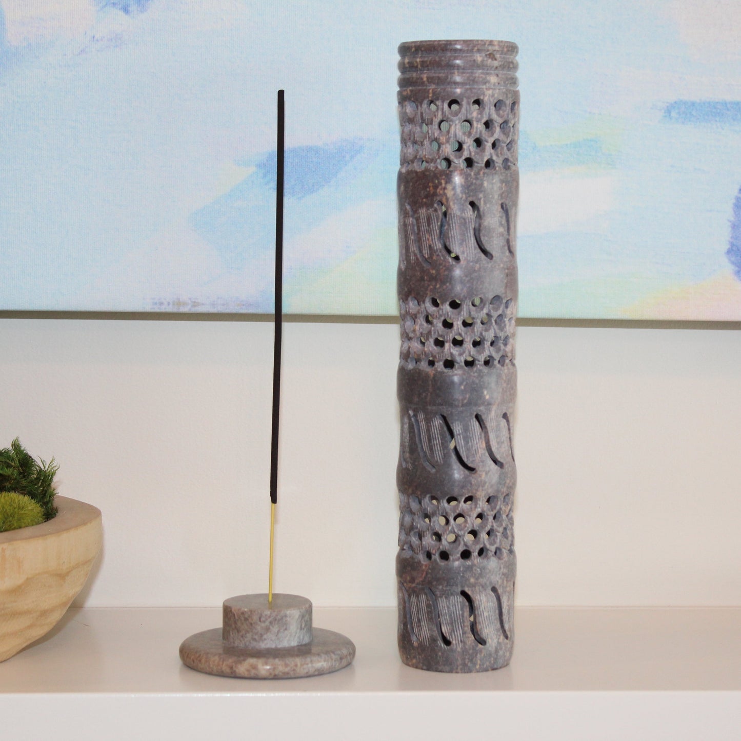 Decorative incense holder with a single incense stick on a shelf with a blurred background