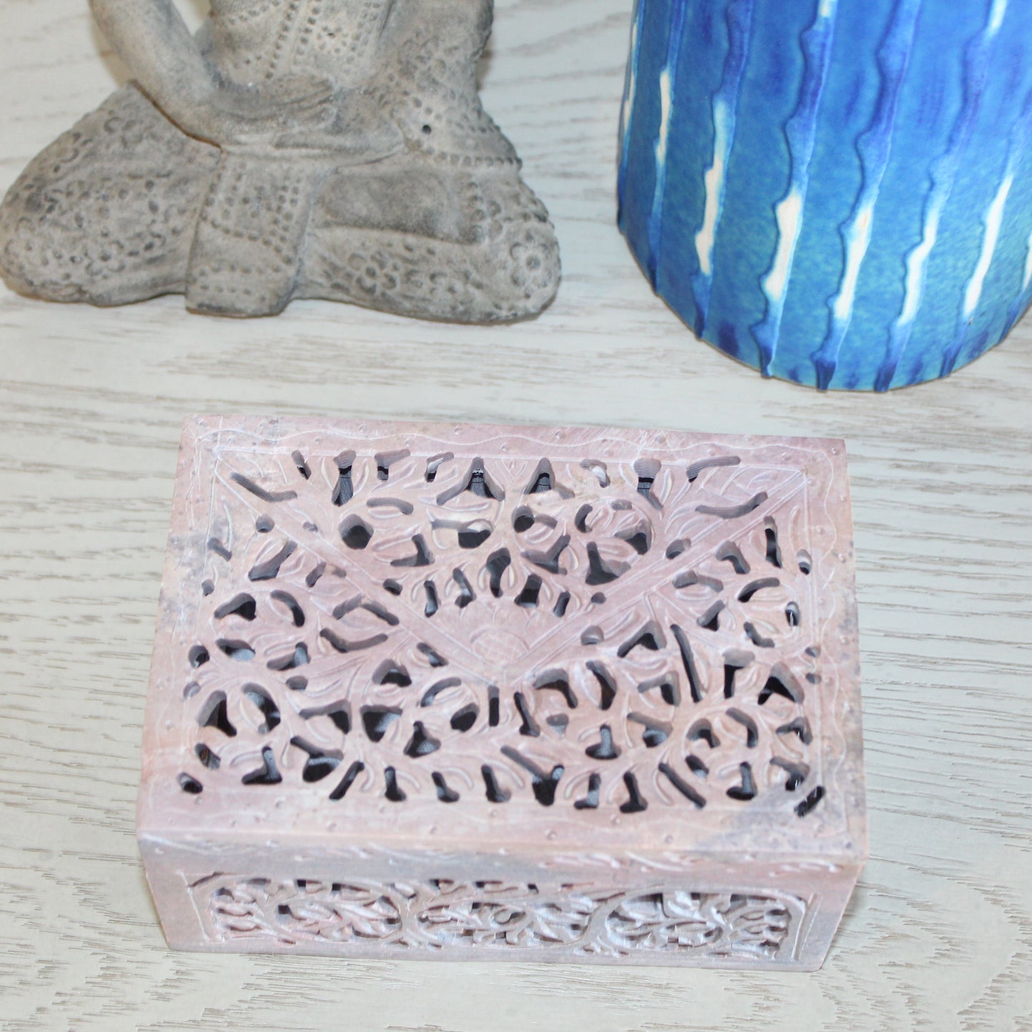 Decorative box with intricate cut-out design on a textured surface with a candle and statue.
