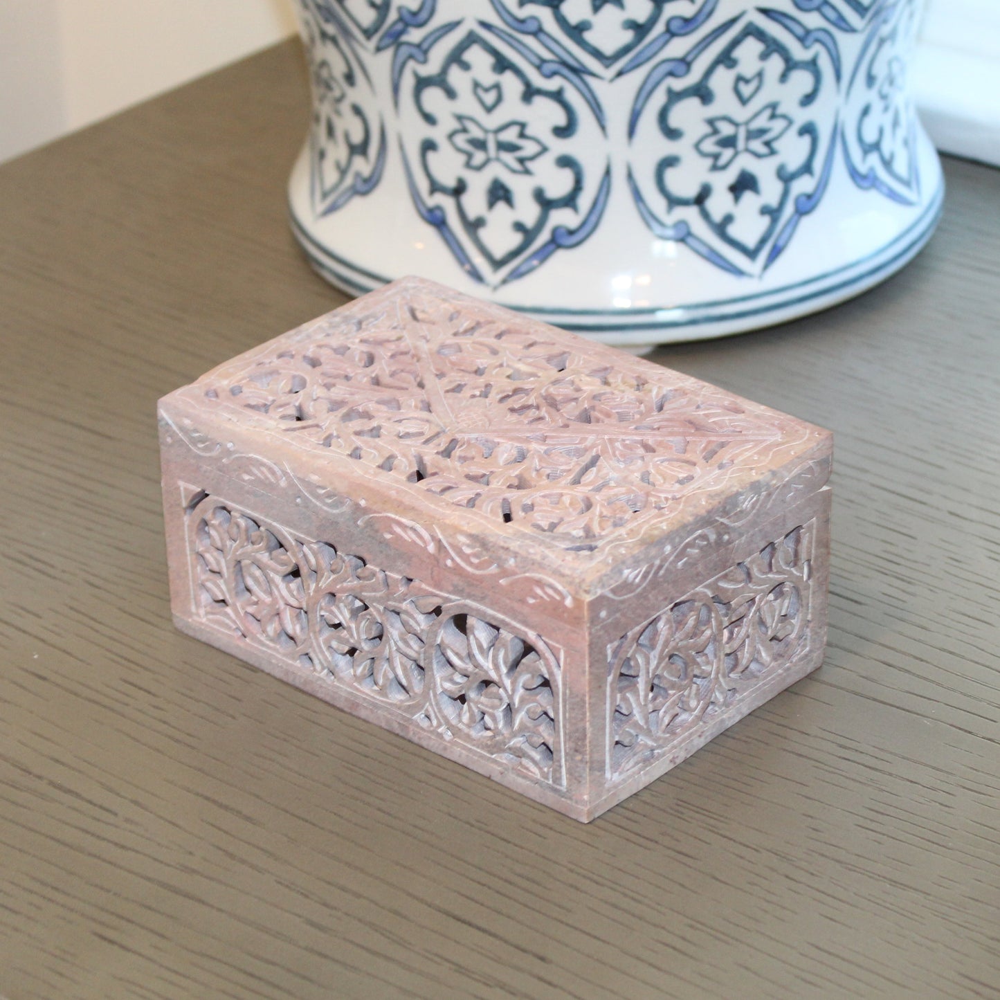 Decorative stone box on a wooden surface with patterned vases in the background