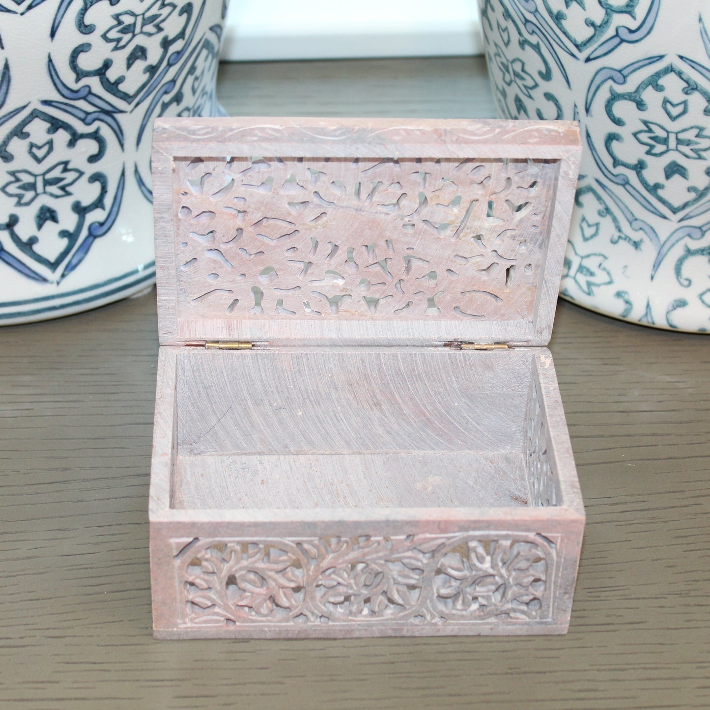 Wooden jewelry box with intricate carvings on a wooden surface with decorative vases in the background.