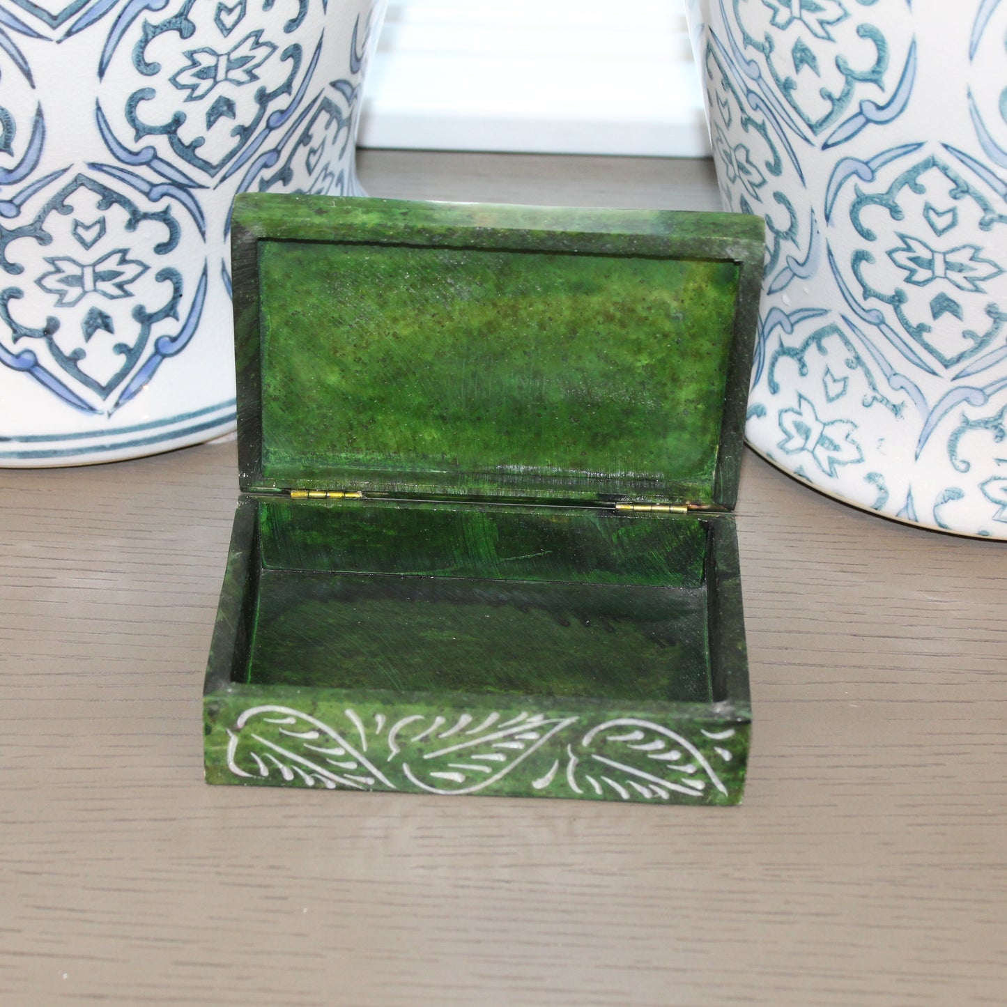Green decorative box with white patterns on a wooden surface with patterned stools in the background.
