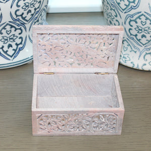 Wooden jewelry box with intricate carvings on a wooden surface with decorative vases in the background.