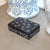 Black decorative box with white patterns on a wooden surface with blue and white ceramic items in the background.