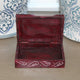 Open red jewelry box with intricate designs on a wooden surface with decorative vases in the background.