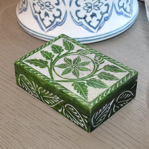 Green decorative box with floral patterns on a wooden surface