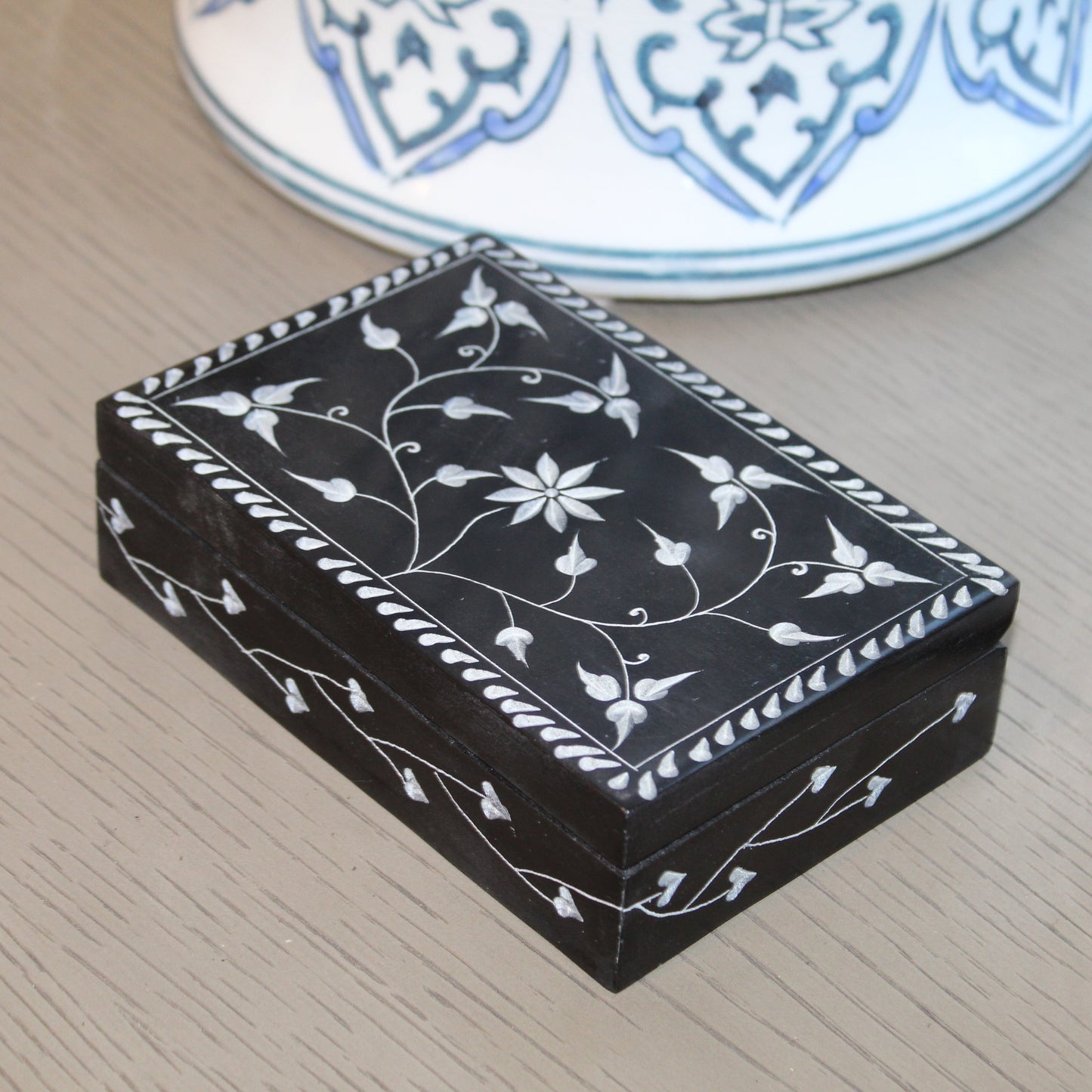 Decorative black box with white floral patterns on a wooden surface